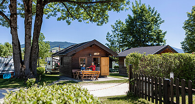 Ältere Dame übergibt Teller an älteren Mann am Eingang der Ferienhütte im Camp Mondseeland