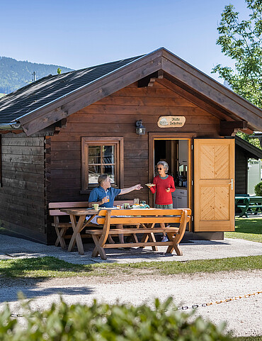 Ferienhütten Ältere Dame übergibt Teller an älteren Mann am Eingang der Ferienhütte im Camp Mondseeland